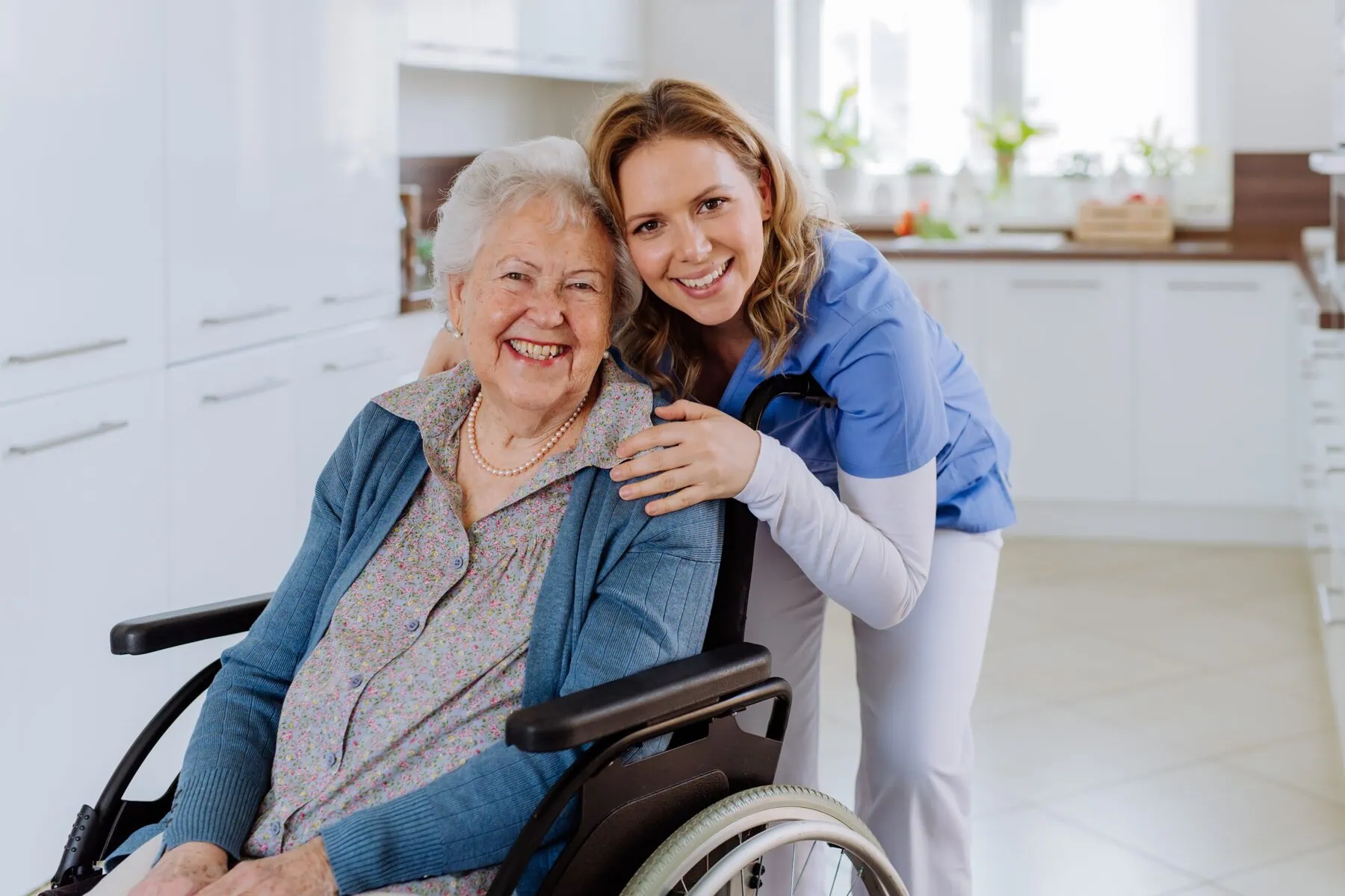 Happy elderly woman in a wheelchair smiling alongside a friendly female caregiver scaled