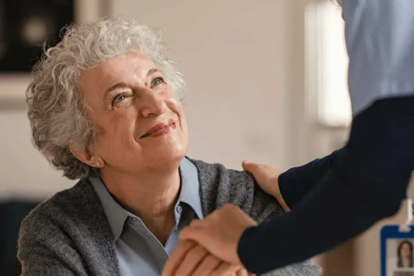Older woman smiling and holding hands with a care worker during a home care support visit.